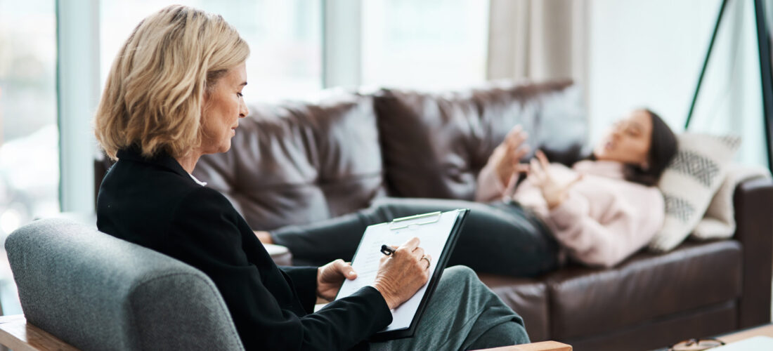 Shot of a mature psychologist writing notes during a therapeutic session with her patient